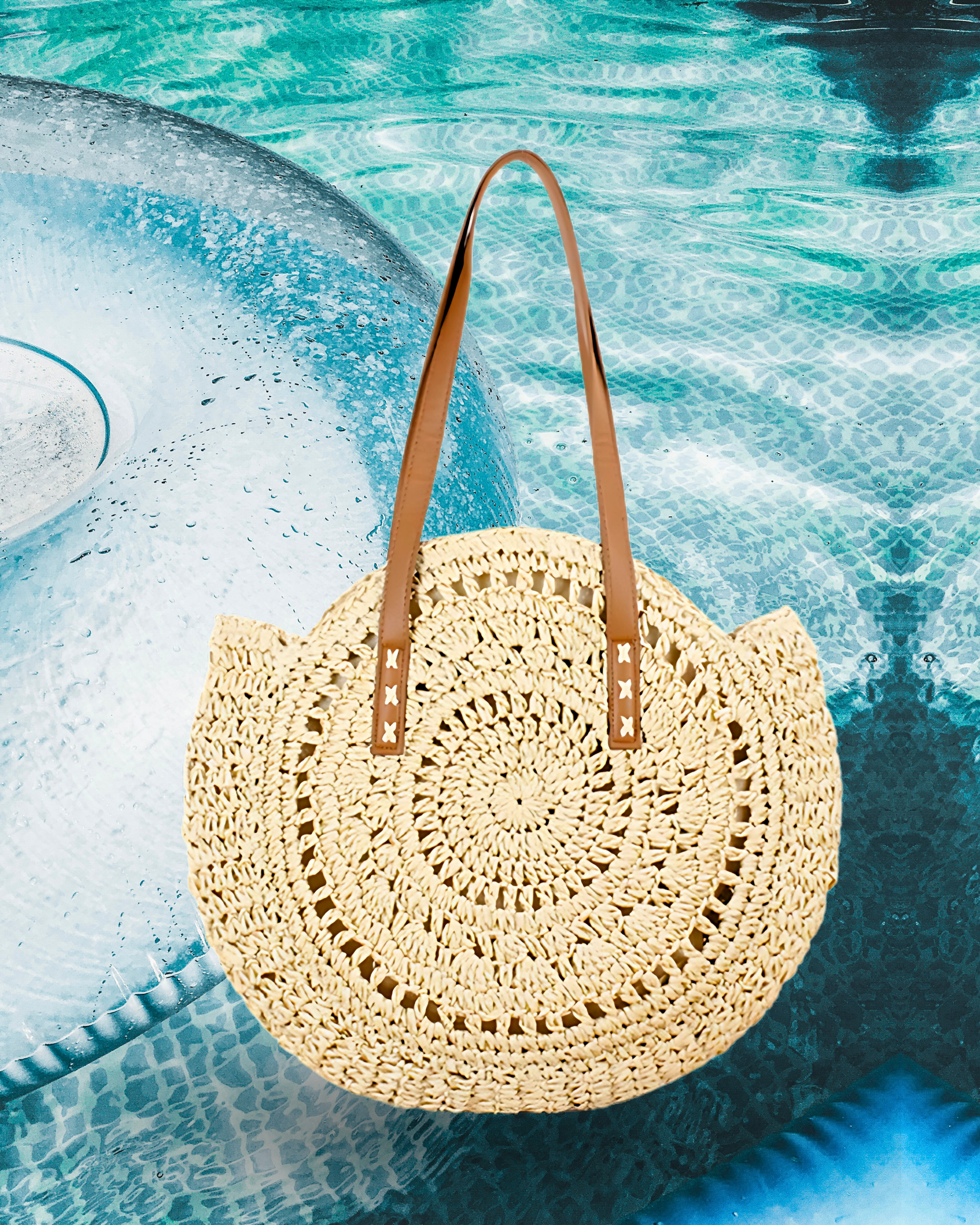 Round woven raffia tote bag with an open spiral crochet pattern and long brown leather shoulder straps for a casual summer style.