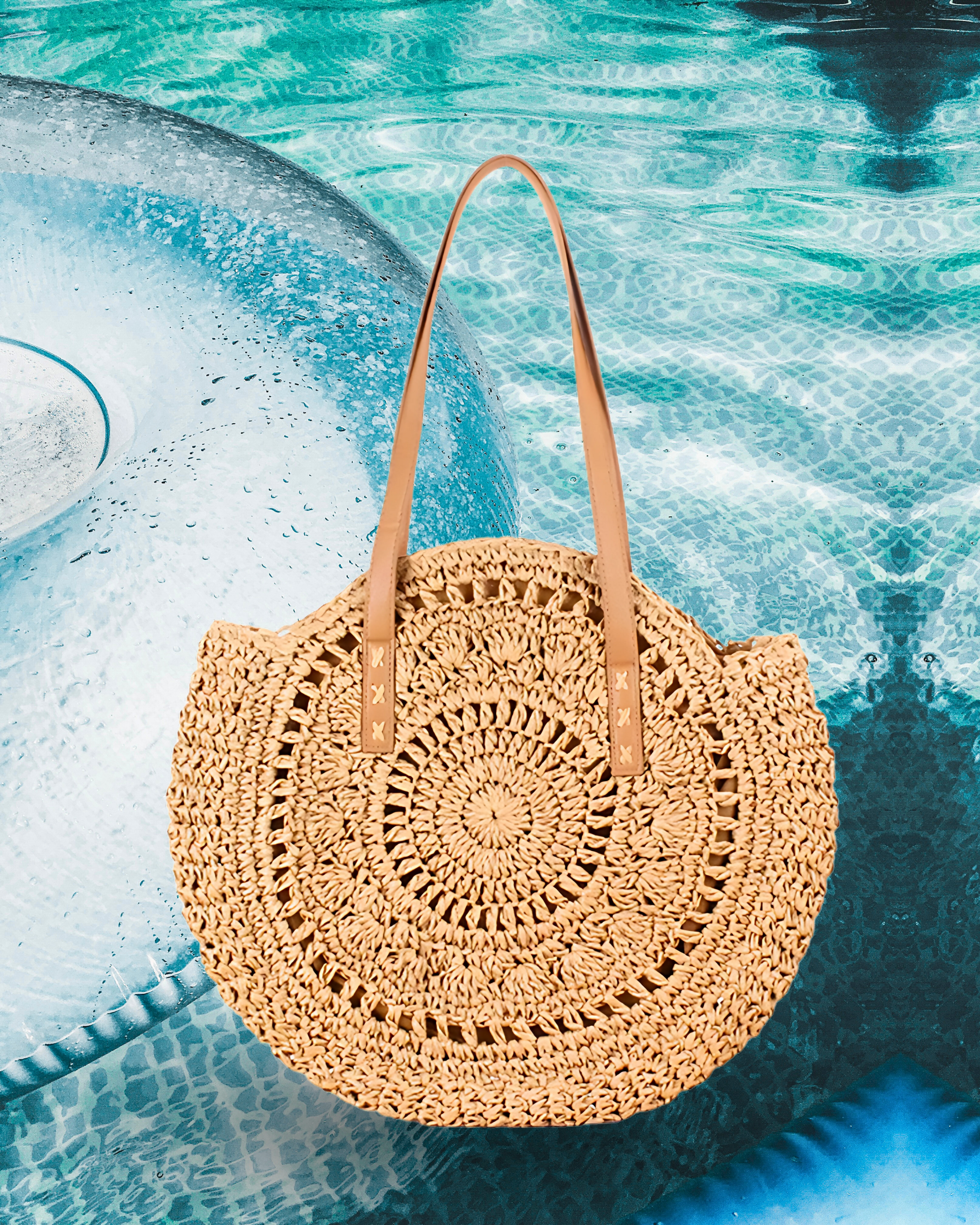 Round woven raffia tote bag with an open spiral crochet pattern and long brown leather shoulder straps for a casual summer style.