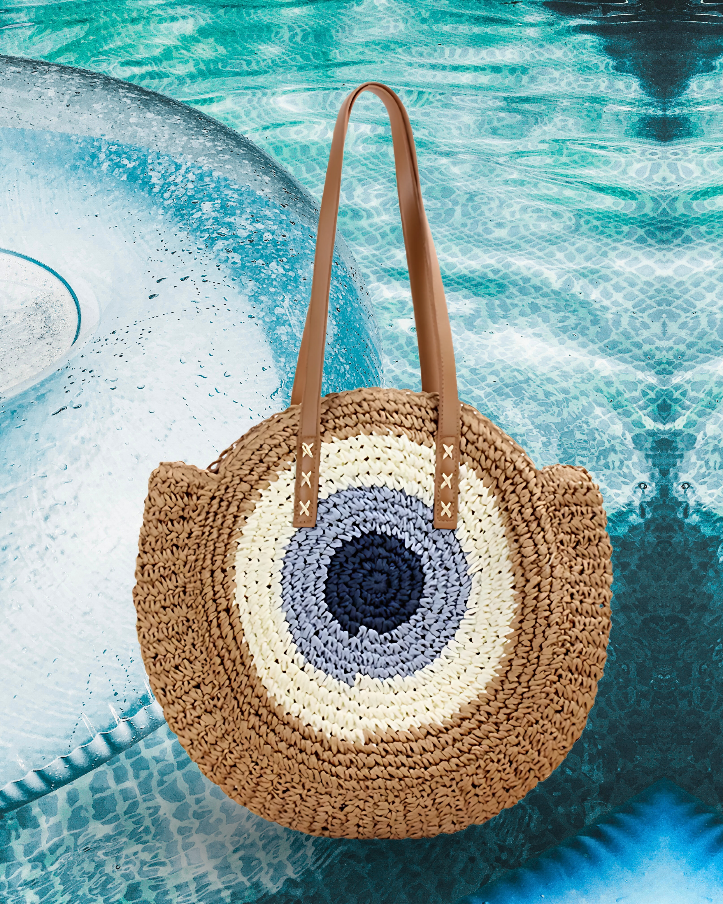 Round woven raffia tote bag with an evil eye design in navy, light blue, beige including long brown leather shoulder straps.