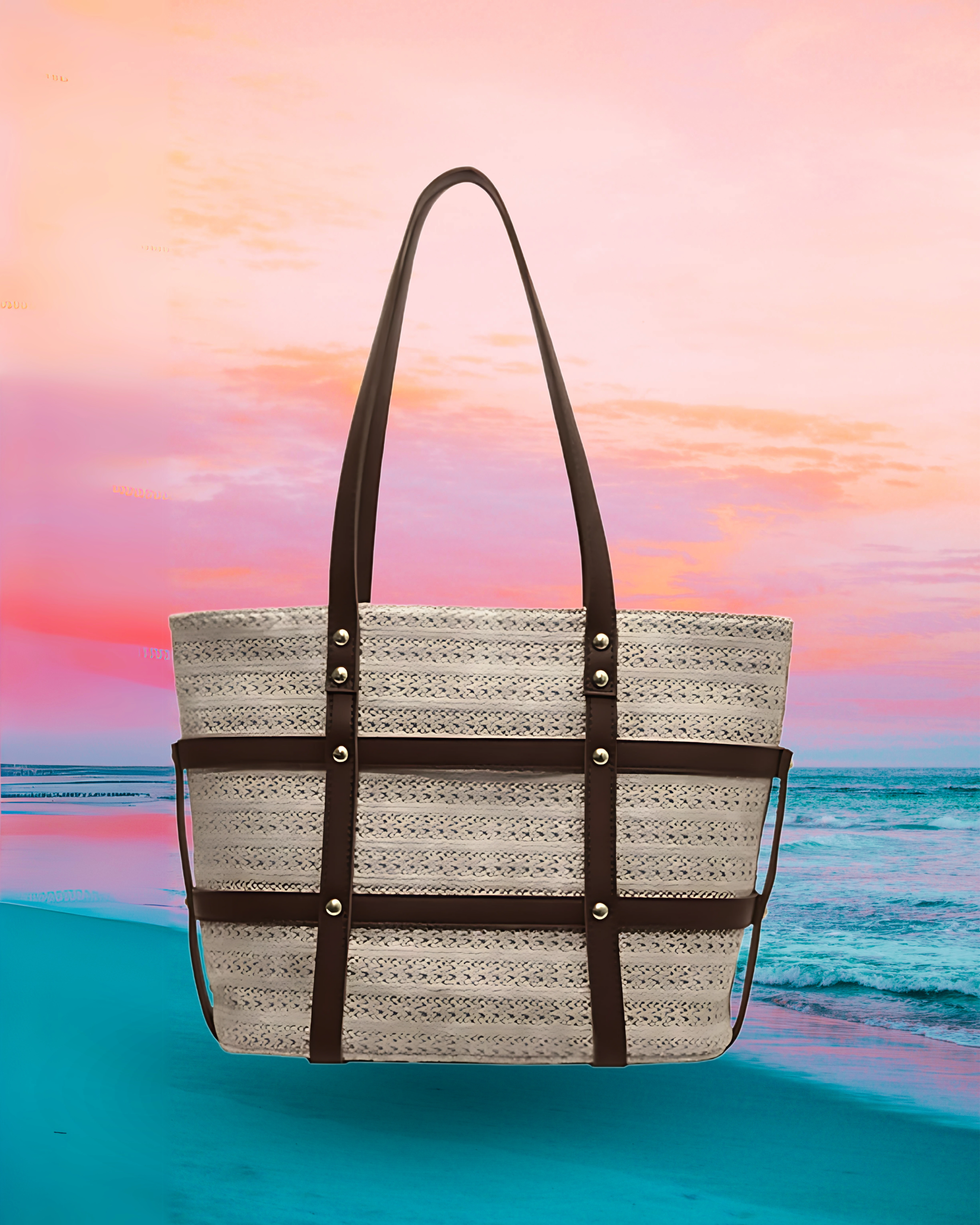 Large rectangular woven raffia tote bag with a structured boxy silhouette, reinforced brown leather straps and trim with gold rivet details, and long dual shoulder handles.