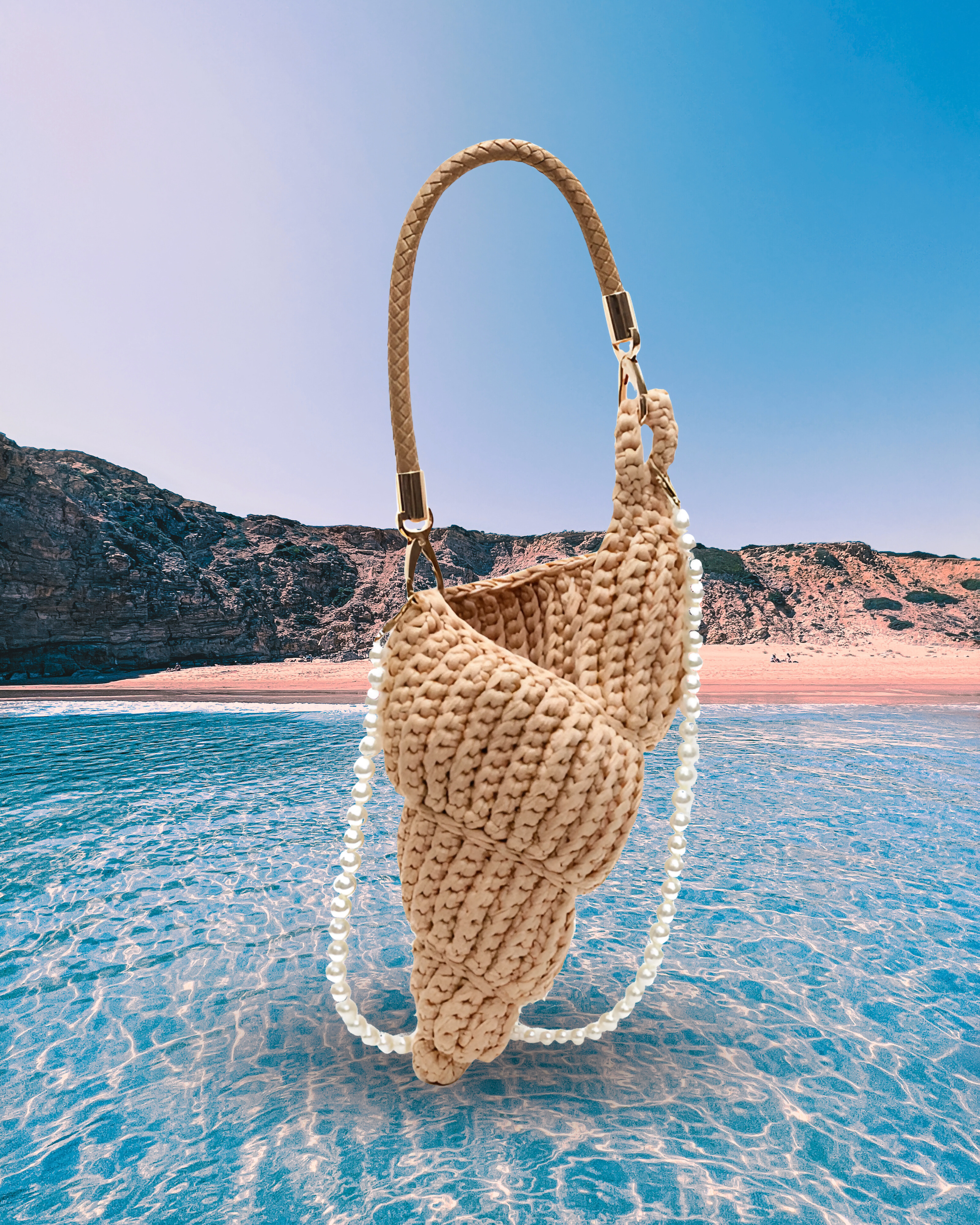 Handwoven beige handbag in a sculptural shell-inspired shape with a braided handle and detachable pearl chain strap for a playful, artistic design.
