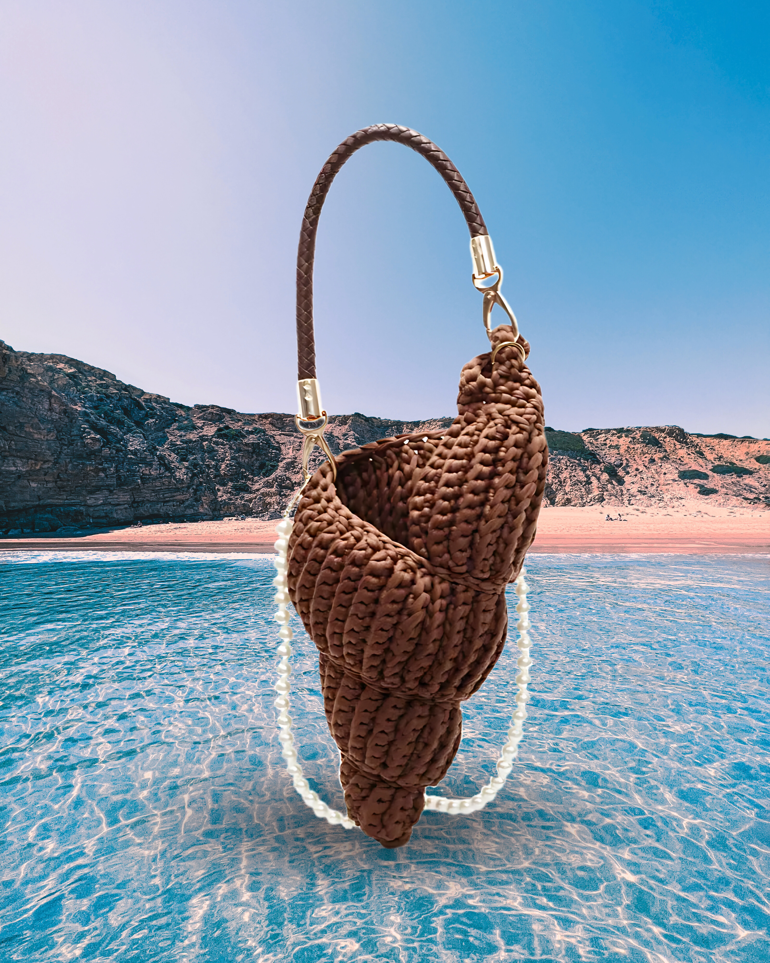 Handwoven brown handbag in a sculptural shell-inspired shape with a braided handle and detachable pearl chain strap for a playful, artistic design.