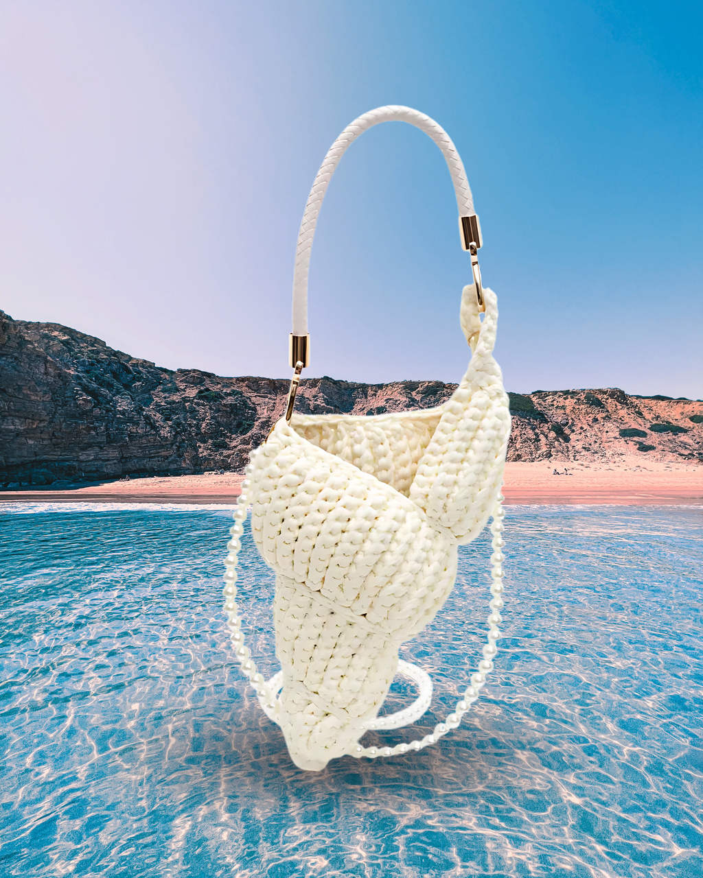 Handwoven cream handbag in a sculptural shell-inspired shape with a braided handle and detachable pearl chain strap for a playful, artistic design.