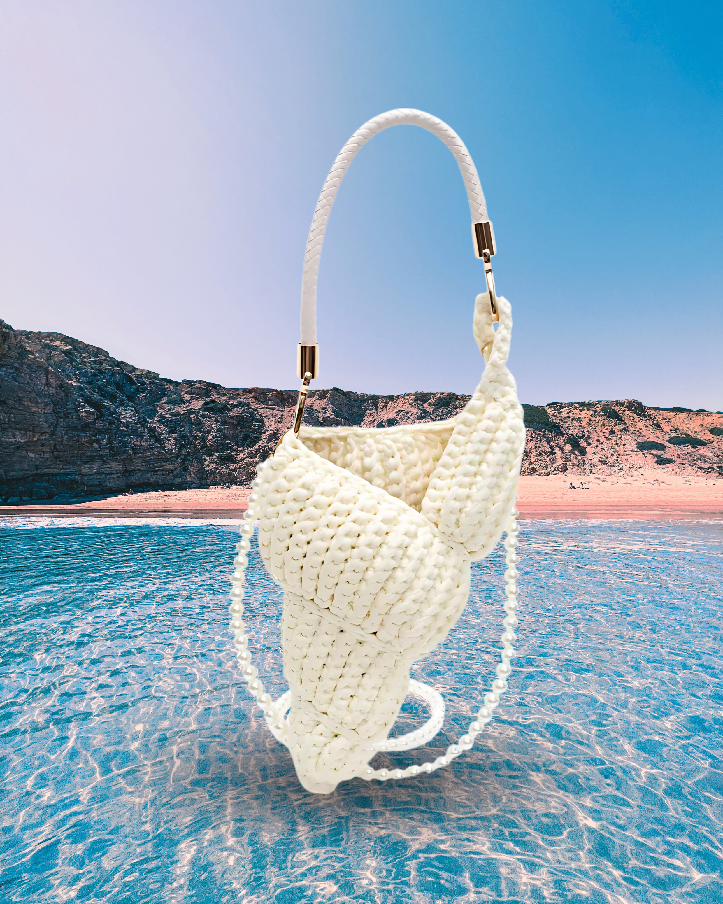 Handwoven cream handbag in a sculptural shell-inspired shape with a braided handle and detachable pearl chain strap for a playful, artistic design.