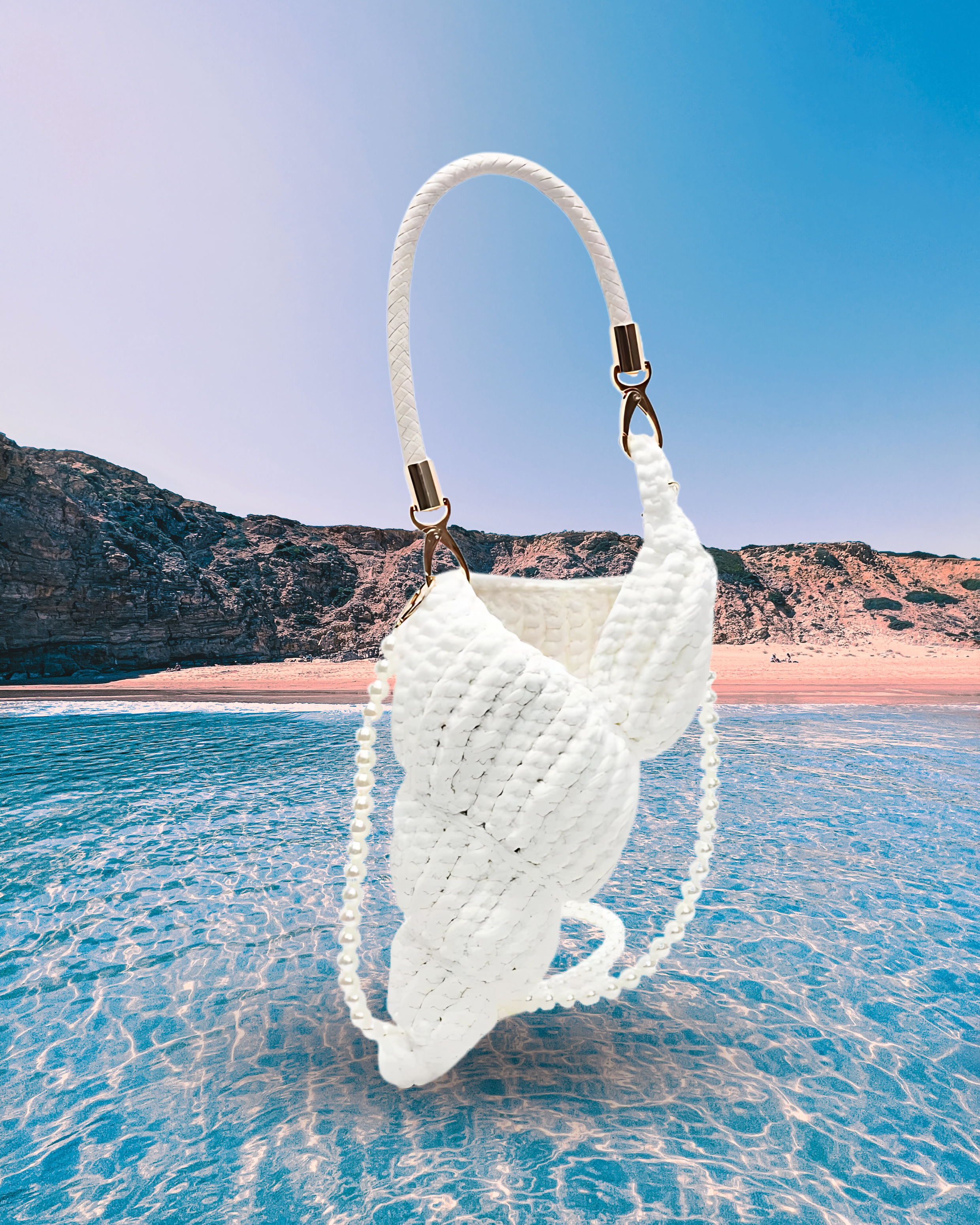 Handwoven white handbag in a sculptural shell-inspired shape with a braided handle and detachable pearl chain strap for a playful, artistic design.