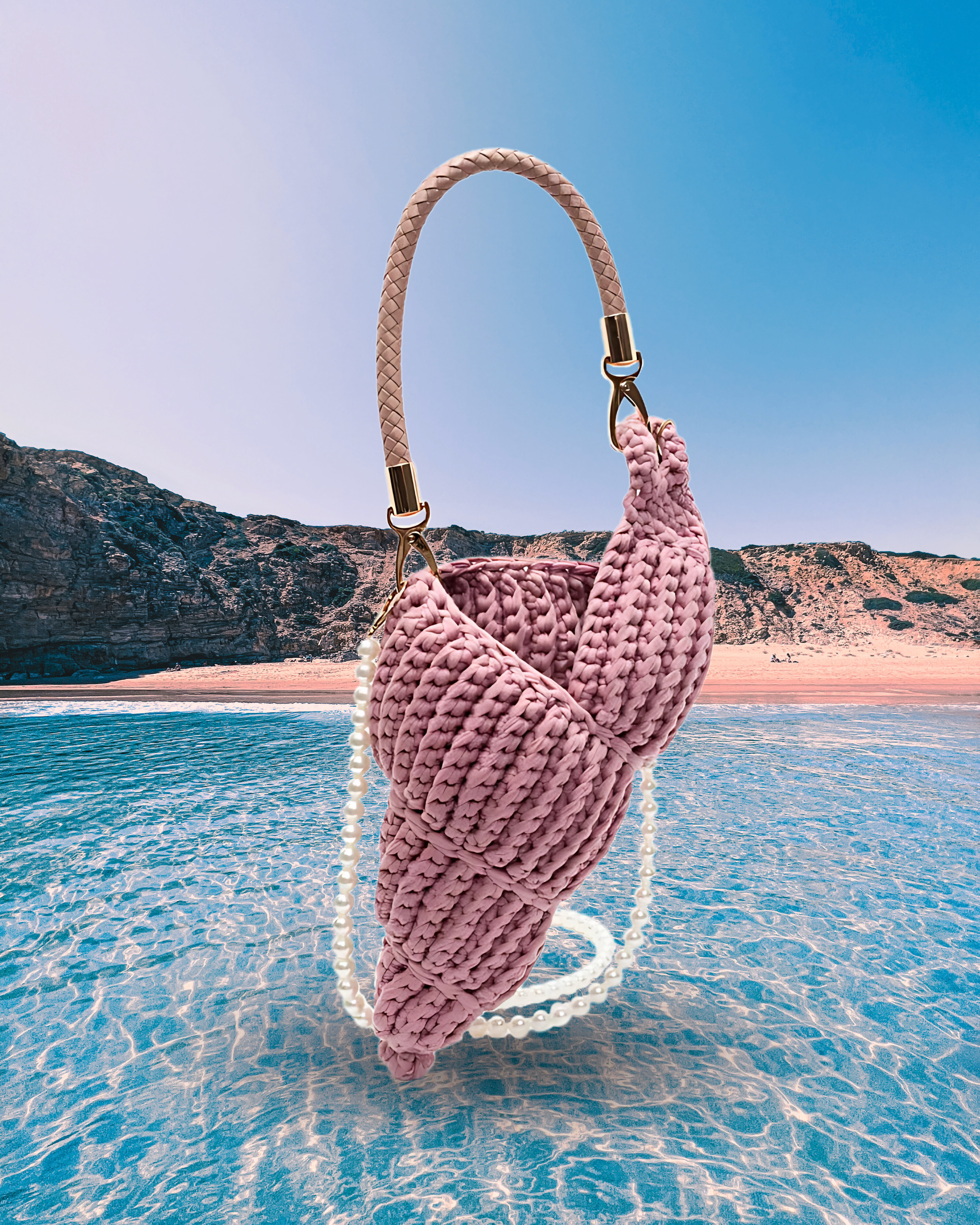 Handwoven pink handbag in a sculptural shell-inspired shape with a braided handle and detachable pearl chain strap for a playful, artistic design.